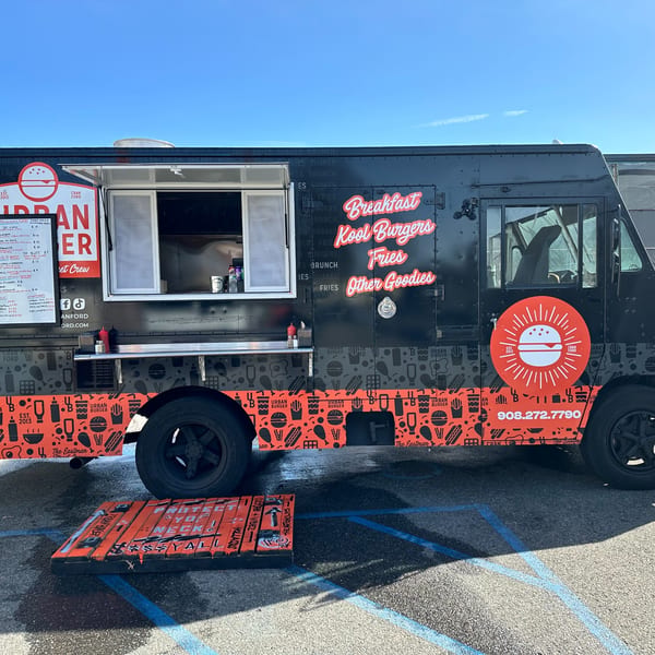 Urban Burger's black food truck with red and white branding, parked on asphalt with a menu board.