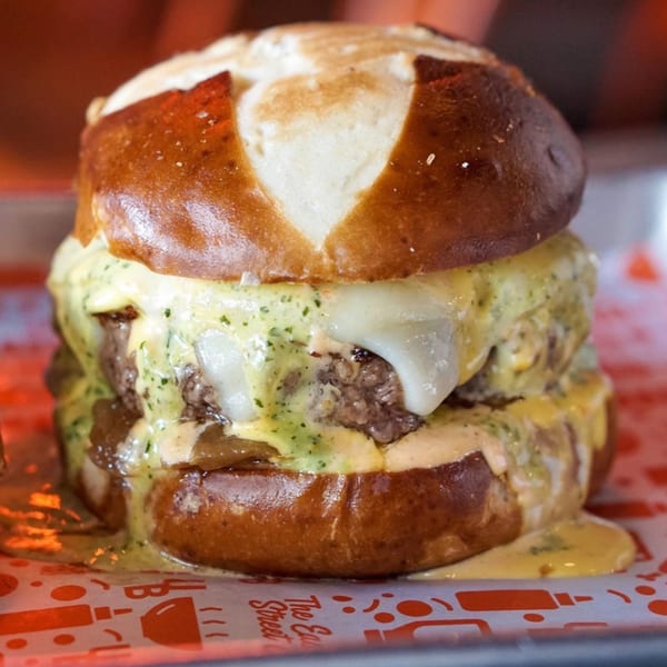 A large Urban Burger with melted cheese and sauces on a pretzel bun, on branded paper.