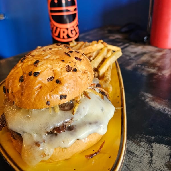 Urban Burger's cheesy burger with fries on a yellow plate, with a branded drink in the background.