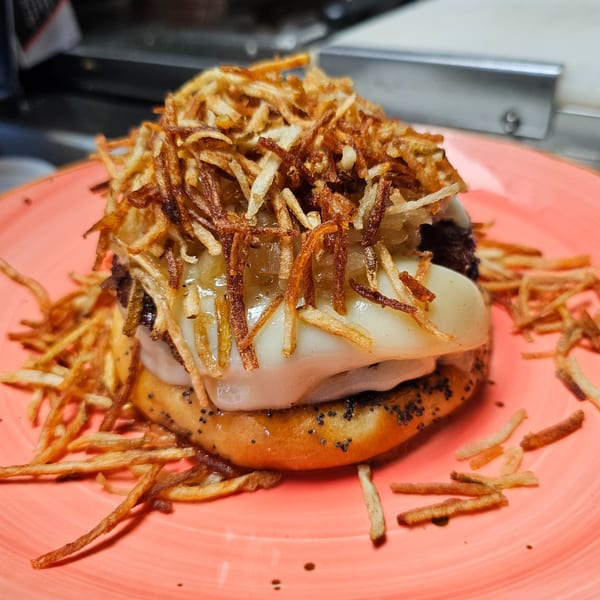 Urban Burger's burger with melted cheese, caramelized onions, and crispy fried potato sticks on a pink plate.