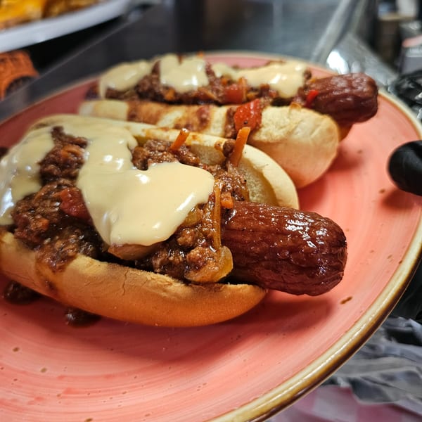 Two chili cheese hot dogs on a pink plate, topped with melted cheese and chili.