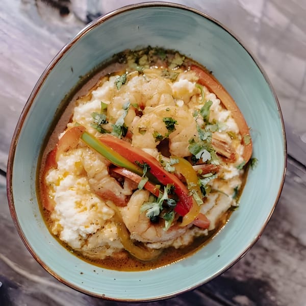 Shrimp and grits with bell peppers and cilantro in a light blue bowl on a wooden table.