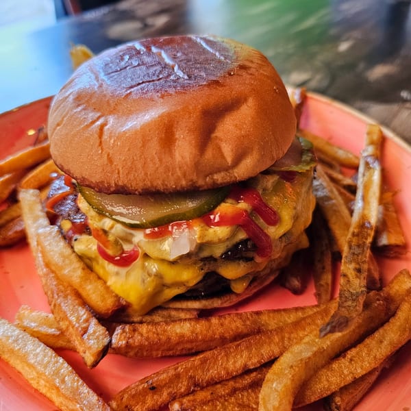 A double cheeseburger with pickles, onions, ketchup, and mayonnaise, served with fries on a red plate.