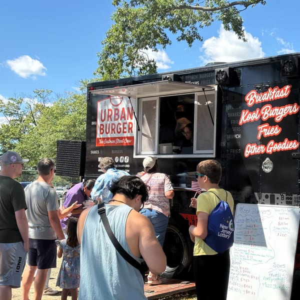 Customers line up at the Urban Burger food truck, featuring a menu board with burger and fries options.